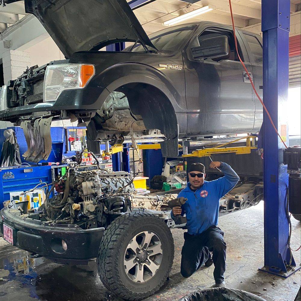 Bo Knows Auto technician kneeling beside a lifted Ford F-150 in the shop