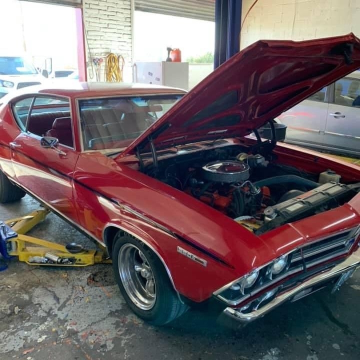 Red classic Chevelle with the hood up on a lift inside the Bo Knows Auto shop