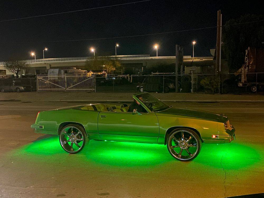 Green Oldsmobile Cutlass convertible with green underglow lighting at night outside the shop